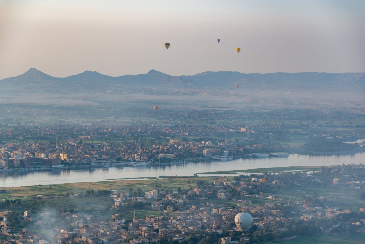 Aerial view of hot air balloons floating over a river and cityscape with mountains in Egypt.